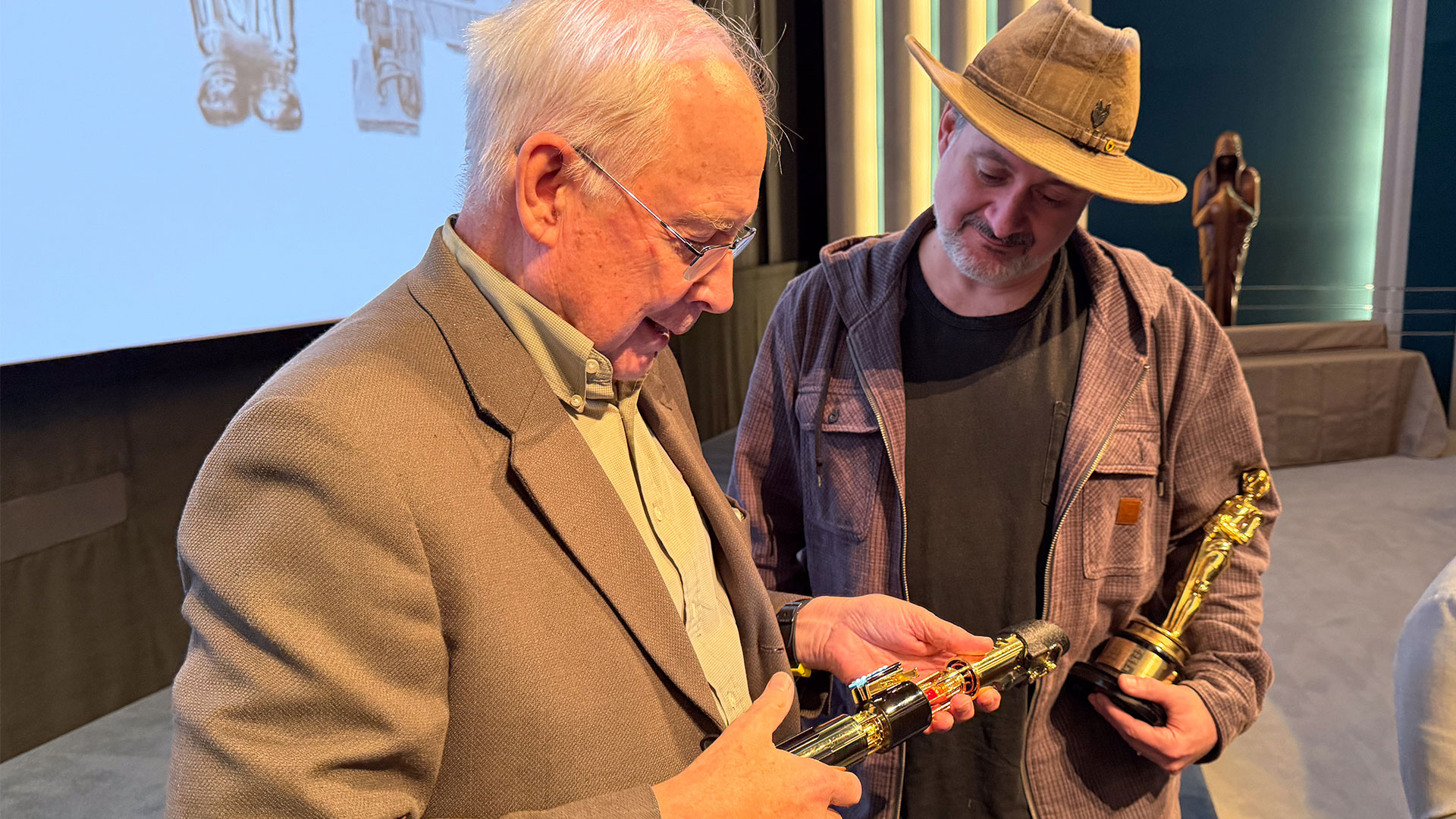 Ben Burtt and Dave Filoni examine Burtt's golden lightsaber service award.